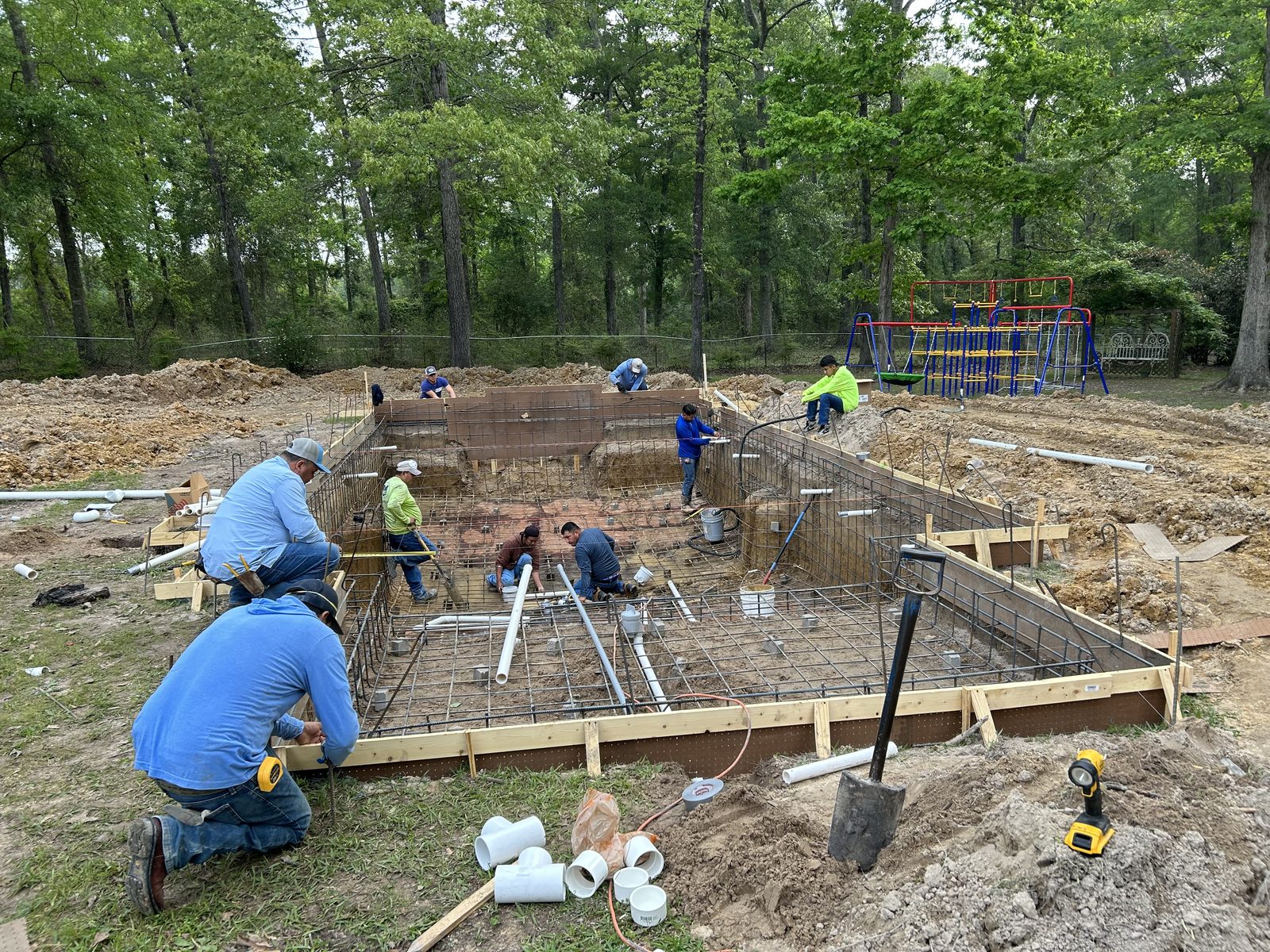 Crew of eight tying the steel reinforcement cage inside an excavated pool before gunite